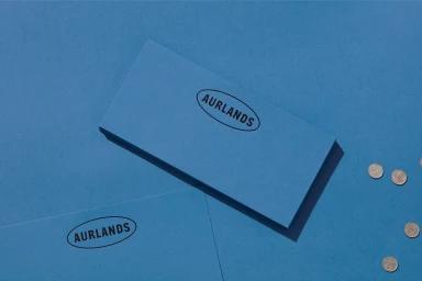 Blue paper stationery set featuring the Aurlands oval logo on a blue background with scattered coins.