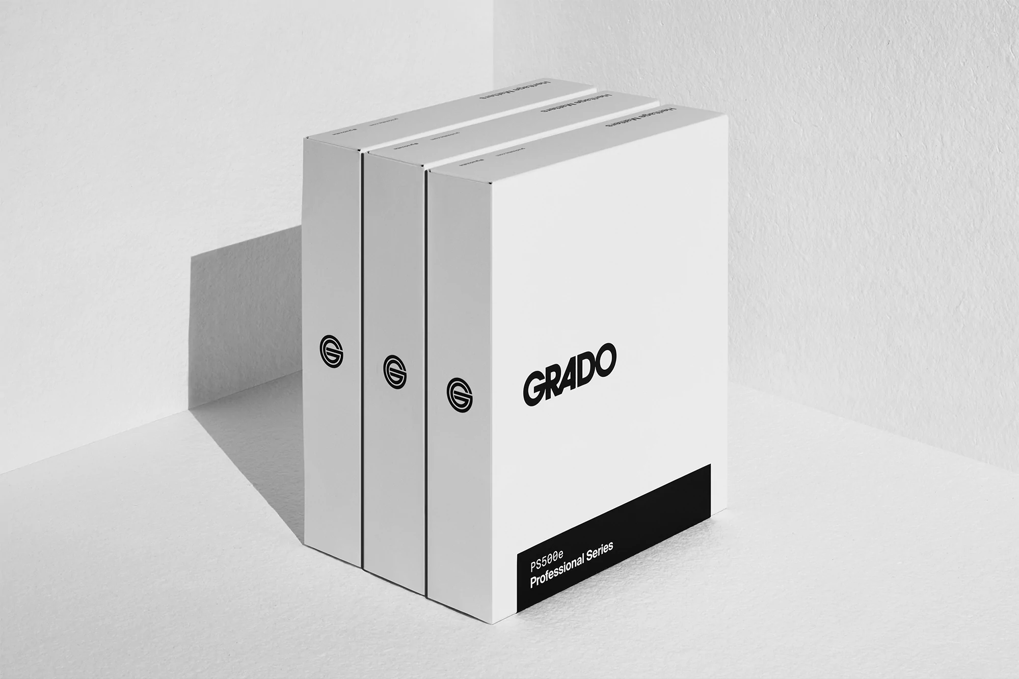Three white boxes with the black Grado logo are stacked against a white wall, creating a clean and minimalist product presentation.