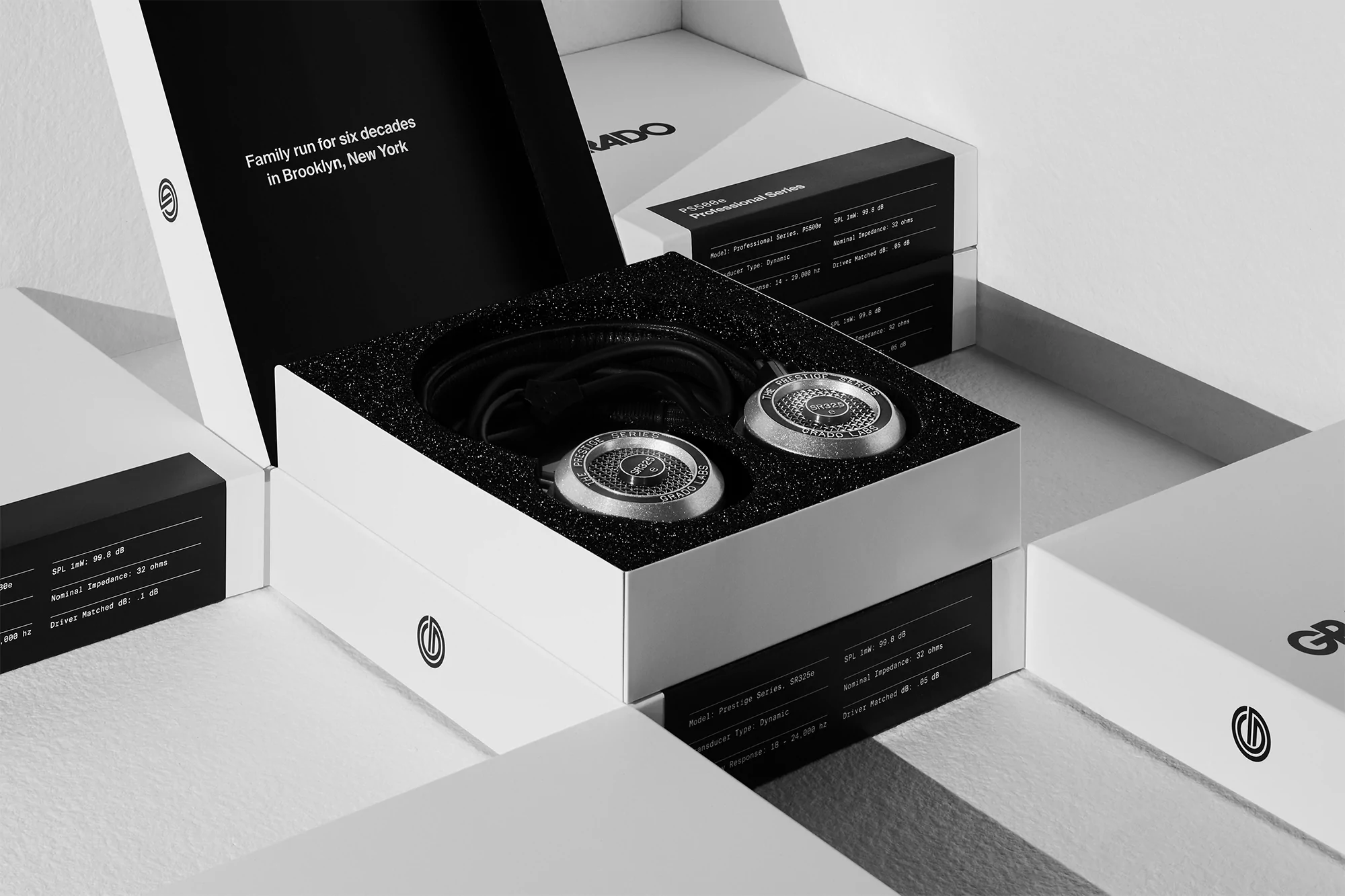 Studio shot of Grado headphones with silver earcups in open white box, specs printed on the box, clean aesthetic, high-quality audio equipment.