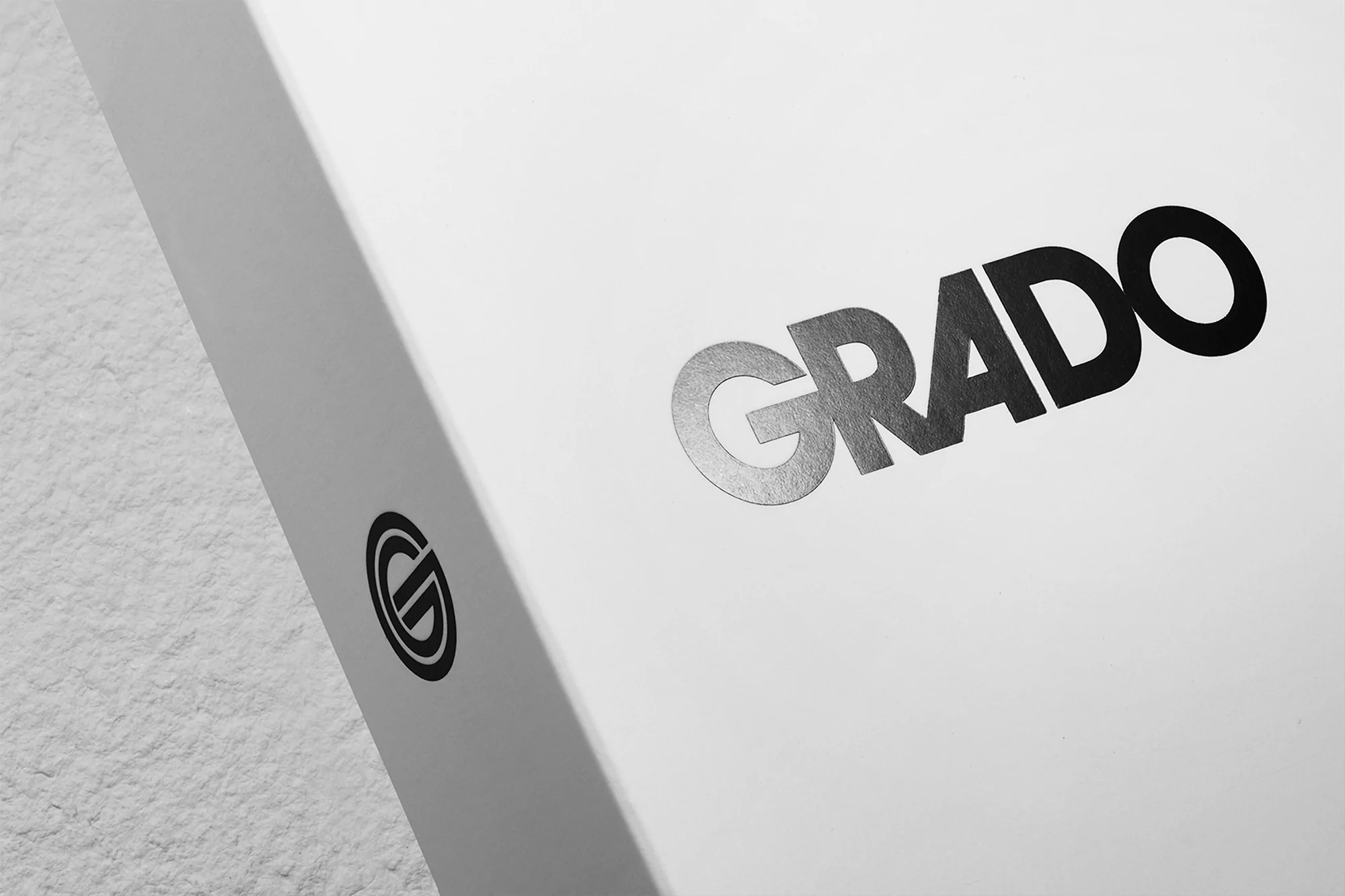 Close-up product shot of a white Grado box featuring the brand name and logo in black. The background is a textured off-white.