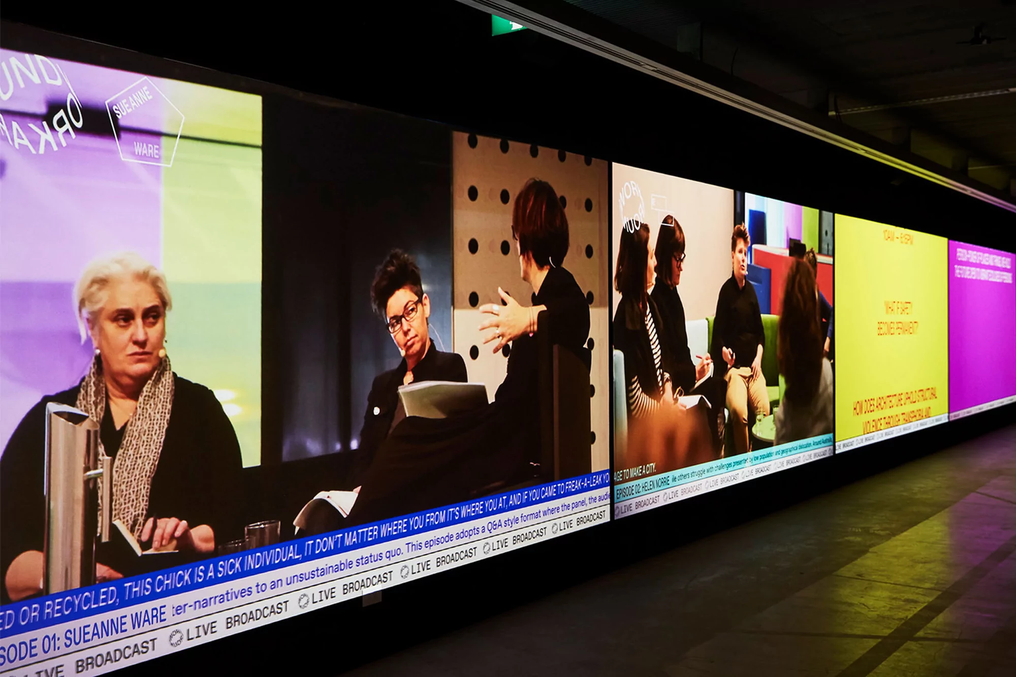 Several people are participating in a panel discussion shown on multiple monitors indoors with text overlays and modern decor.