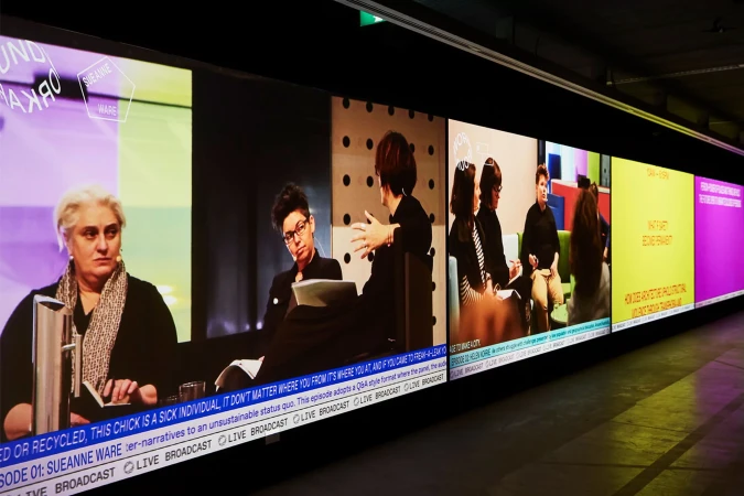Several people are participating in a panel discussion shown on multiple monitors indoors with text overlays and modern decor.