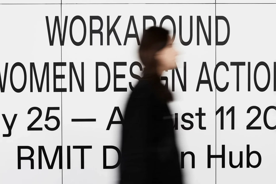 Blurred person walks past large format poster with text 'WORKAROUND WOMEN DESIGN ACTION July 25 – August 11 2024 RMIT Design Hub'.