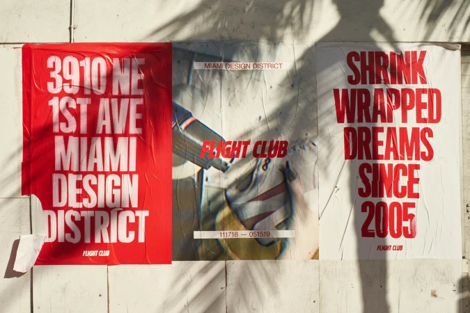 Posters on a wall advertising Flight Club, with a Miami Design District address and dates. Red and white color scheme.