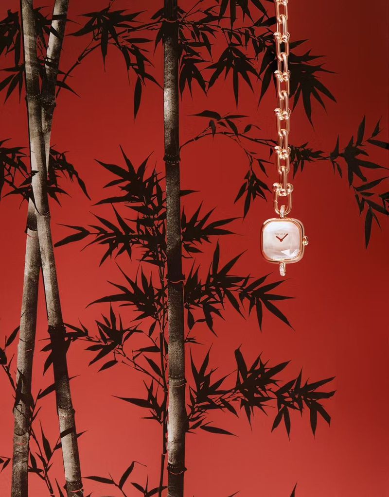 Elegant gold chain watch with square face against a red backdrop with a bamboo leaf pattern, showcasing luxury and design.