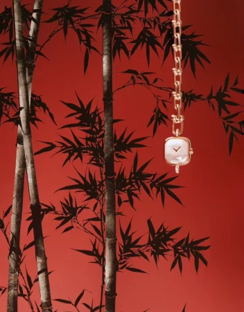 Elegant gold chain watch with square face against a red backdrop with a bamboo leaf pattern, showcasing luxury and design.