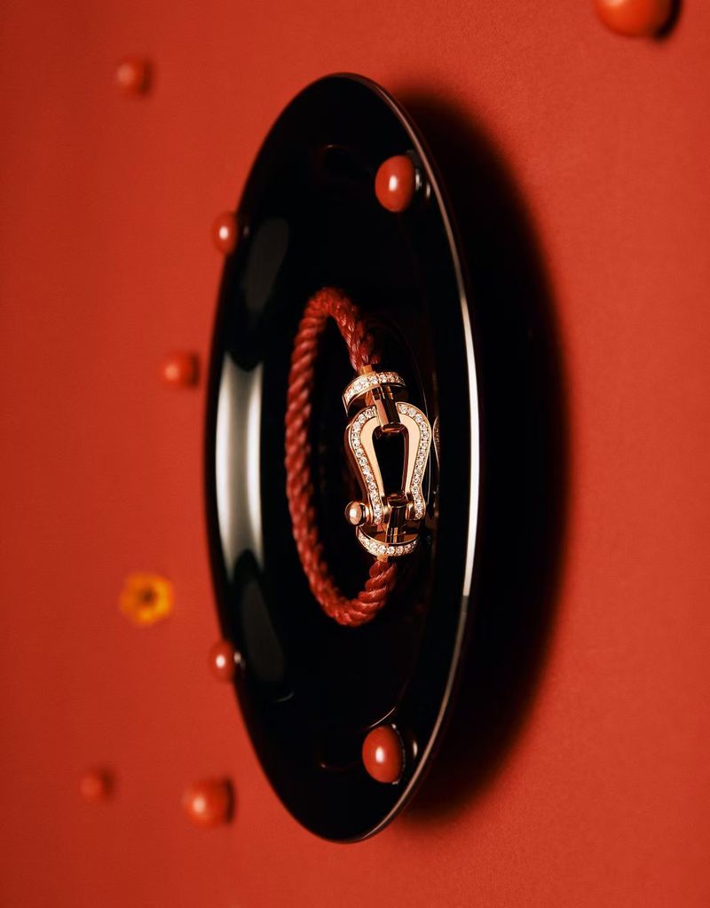 A red bracelet on a glossy black tray, surrounded by small red beads, creates a striking jewelry display against a vibrant red background.