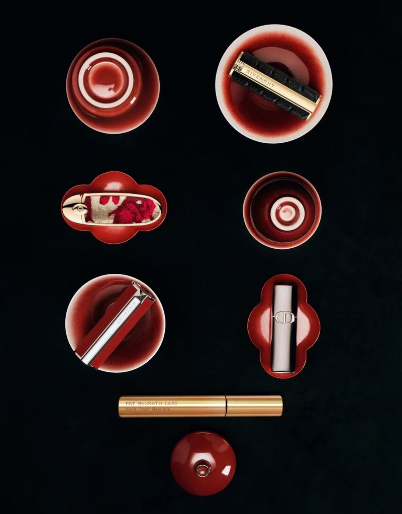 Overhead shot of several red-toned cosmetic containers arranged on a black surface in a high-angle product studio photograph.