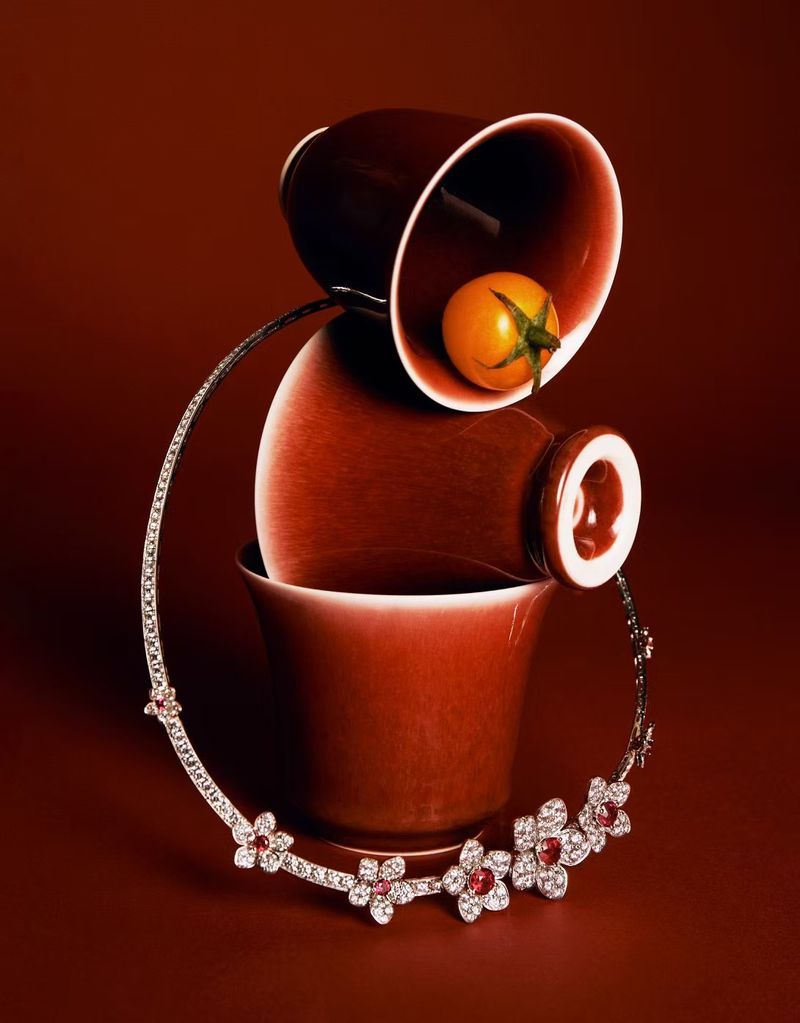 Still life shot featuring a floral diamond necklace draped around terracotta-colored cups, with a single golden tomato inside the top cup.