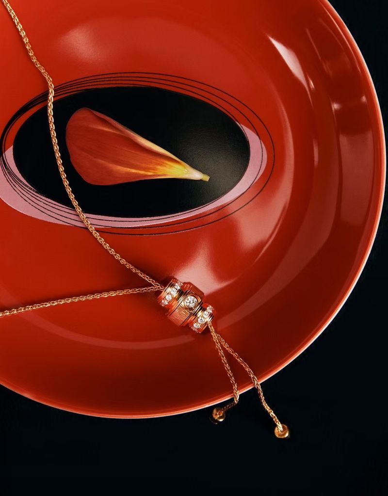 Gold necklace with small circular pendants displayed on a red plate with a petal in the background against a black surface.