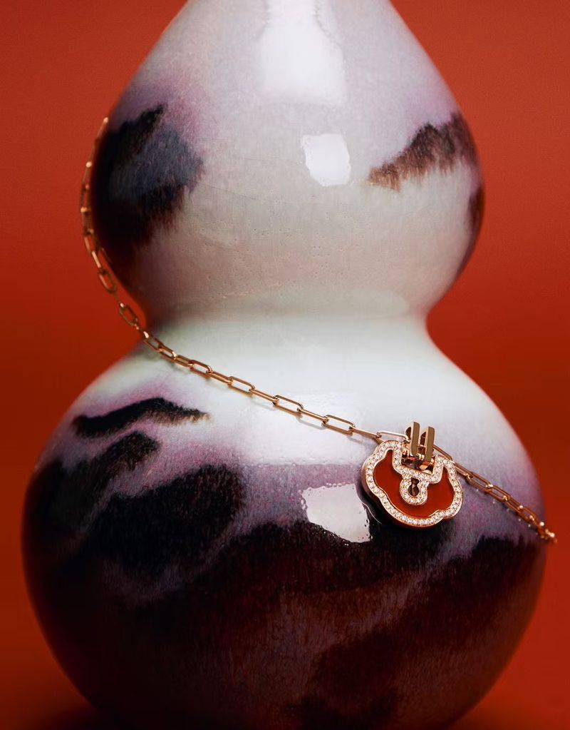 Close-up of a gold chain necklace featuring a red pendant with diamond accents, draped over a patterned, gourd-shaped ceramic vase.