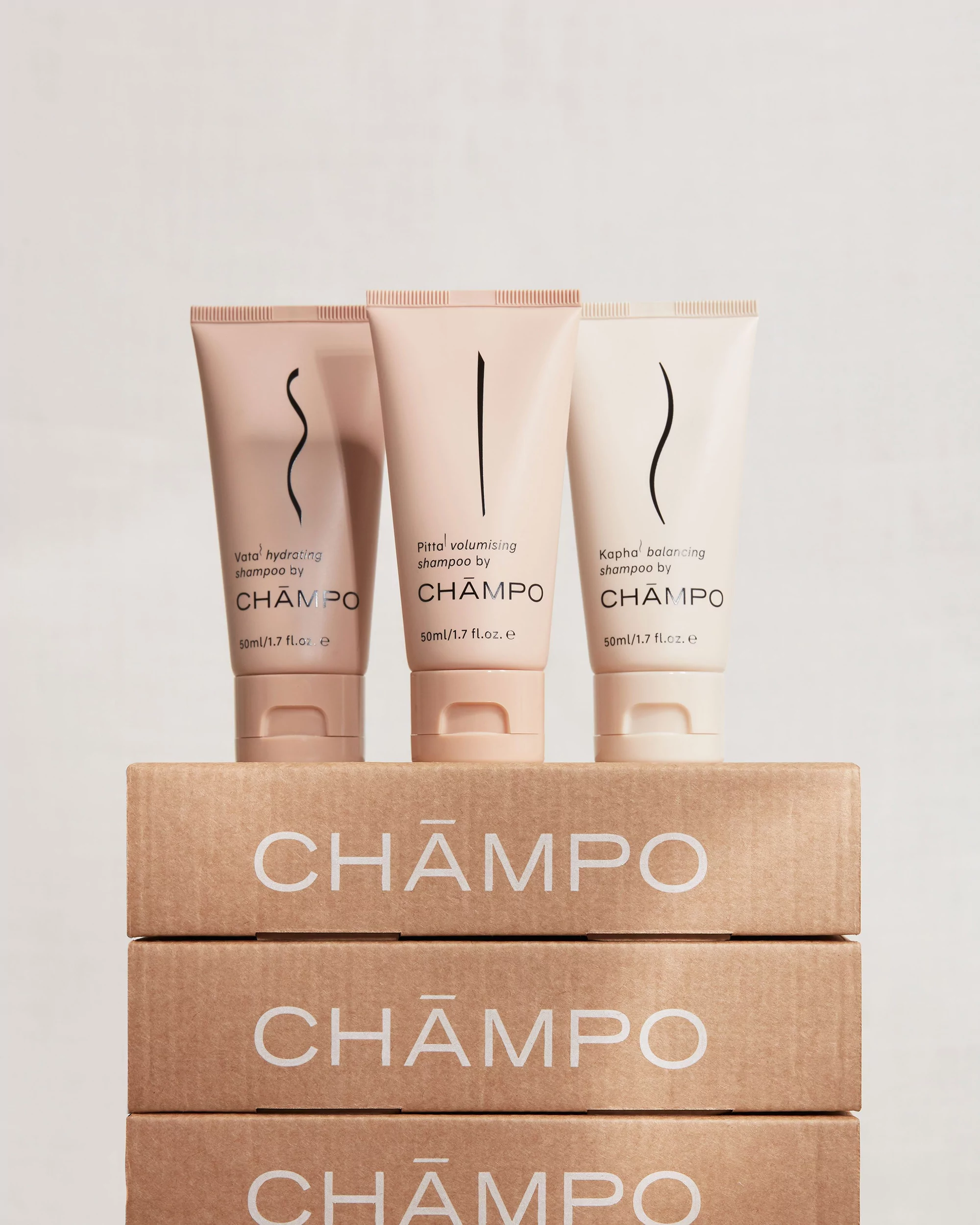 Three CHĀMPŌ shampoo bottles displayed on boxes stacked against a white background, product promotion, and beauty product shot.