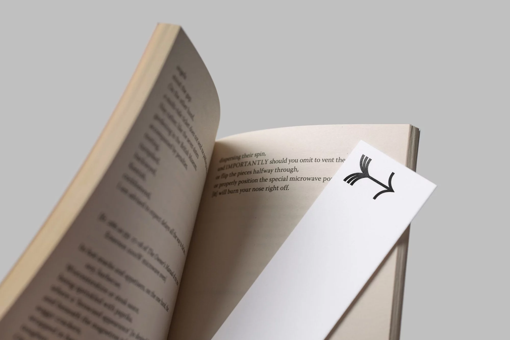 Opened book with a white bookmark featuring a black arrow design, set against a soft grey background in a studio setting.