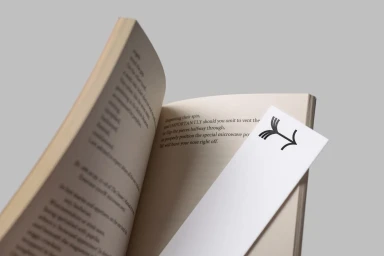 An open book with visible text pages and a white custom branded bookmark placed diagonally against a neutral grey background.