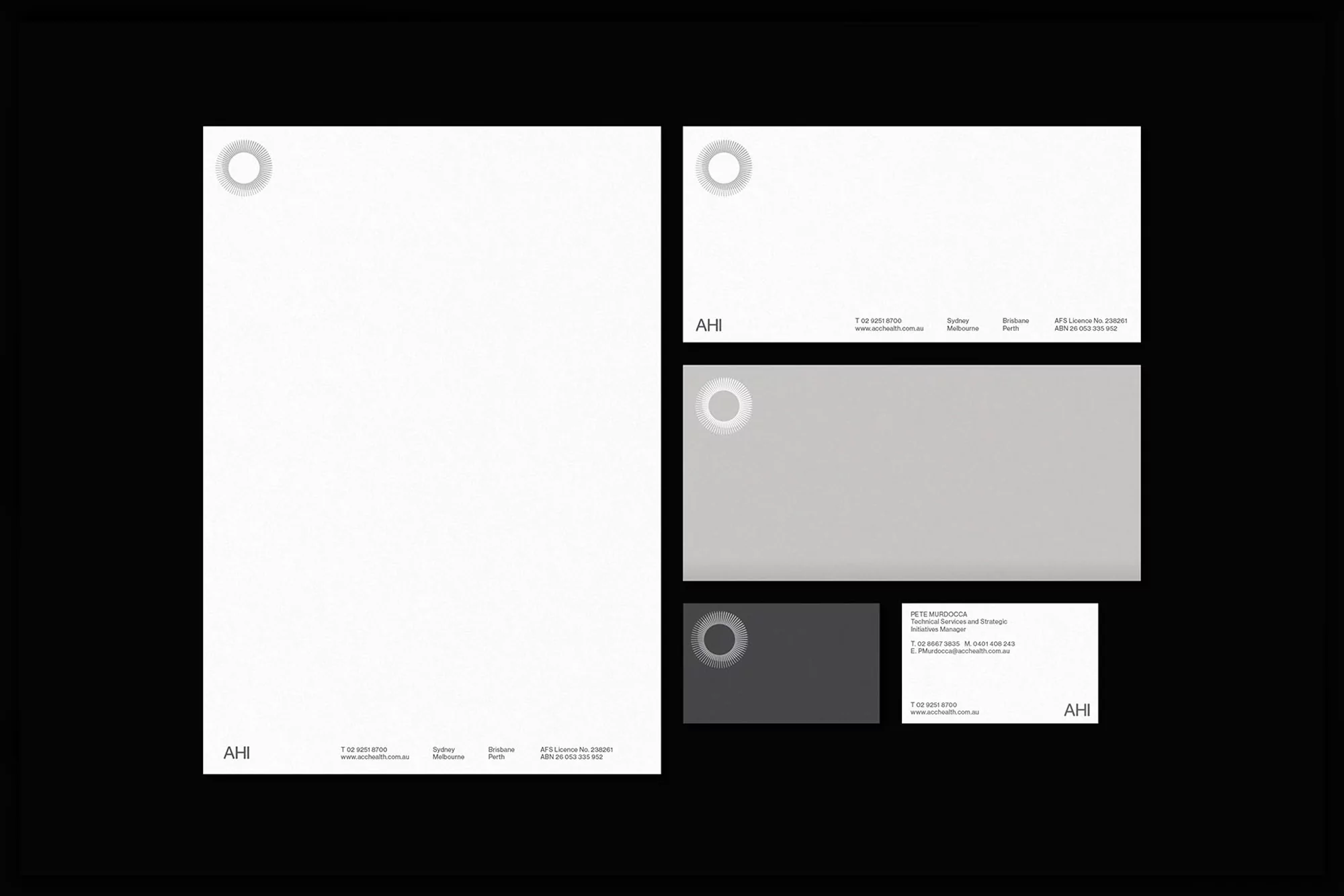 Close-up of AHI branded stationery including letterhead, business card, and notecard, all in white, grey, and black on a black background.