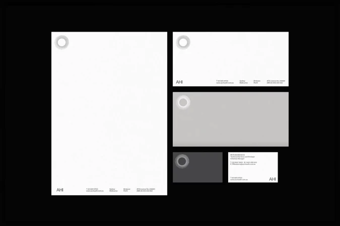 Close-up of AHI branded stationery including letterhead, business card, and notecard, all in white, grey, and black on a black background.