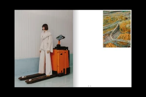 Model standing on a forklift wearing white trousers and a white top next to an orange forklift in an industrial interior.