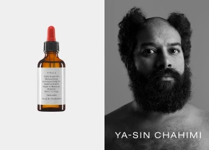 Amber glass cosmetic dropper bottle next to a black and white portrait of a bearded man with stylized hair.