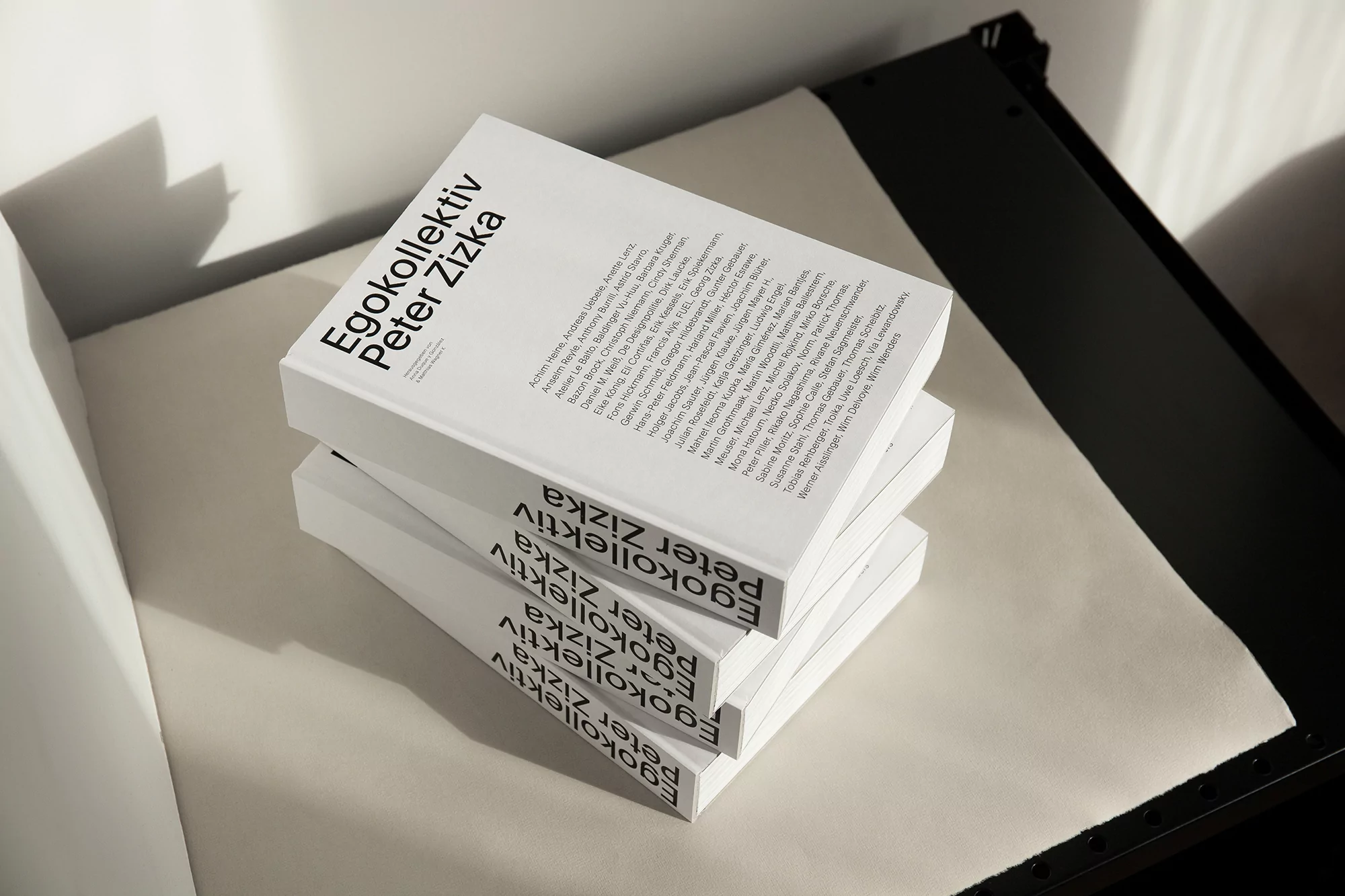 Stack of three books with white covers and black text, casting shadows, positioned on a soft surface in a studio setting.