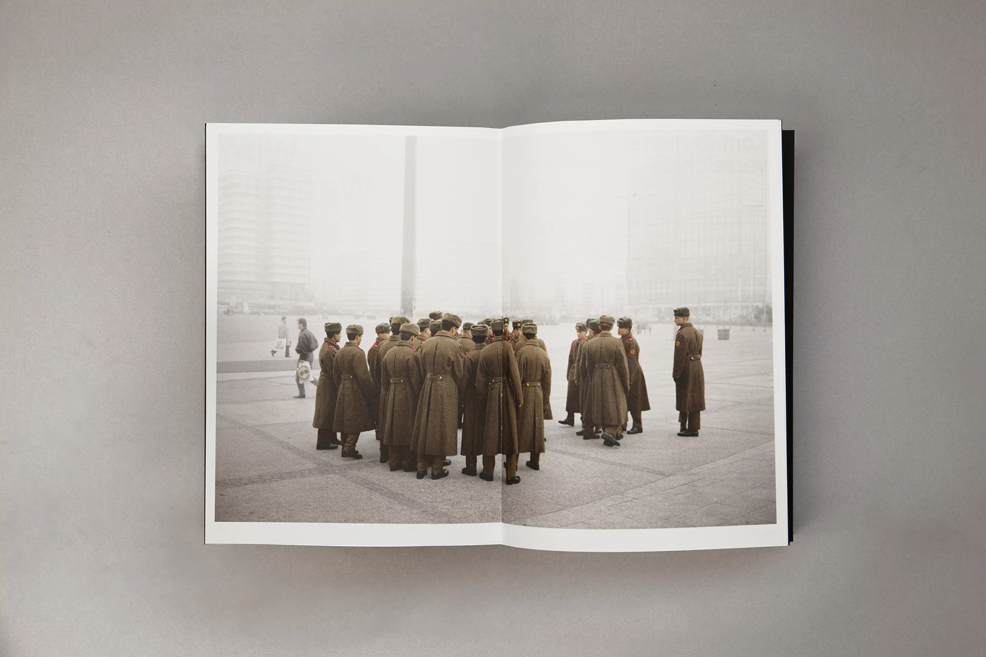 Editorial shot of a large group of soldiers in uniform standing in formation in a city square, viewed in an open book on a gray surface.