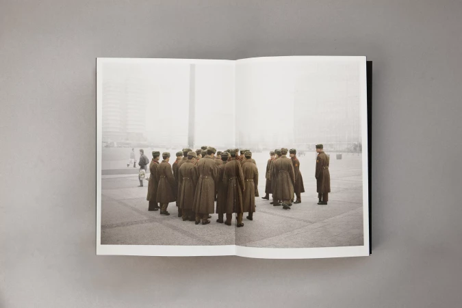 Editorial shot of a large group of soldiers in uniform standing in formation in a city square, viewed in an open book on a gray surface.