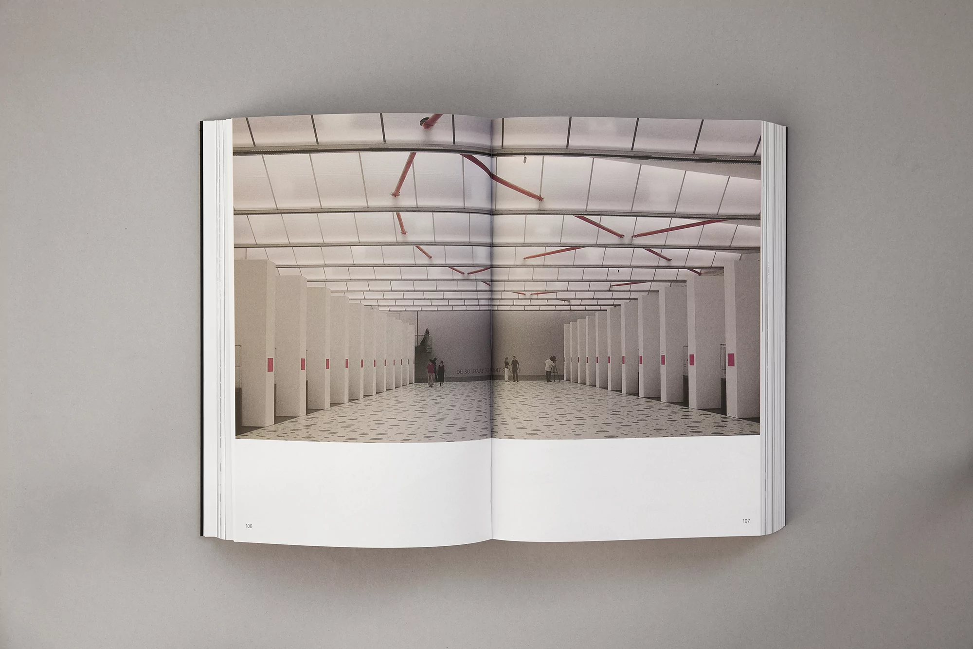 Open book displaying photograph of a large, sparsely populated modern hall with white support columns and geometric flooring pattern.