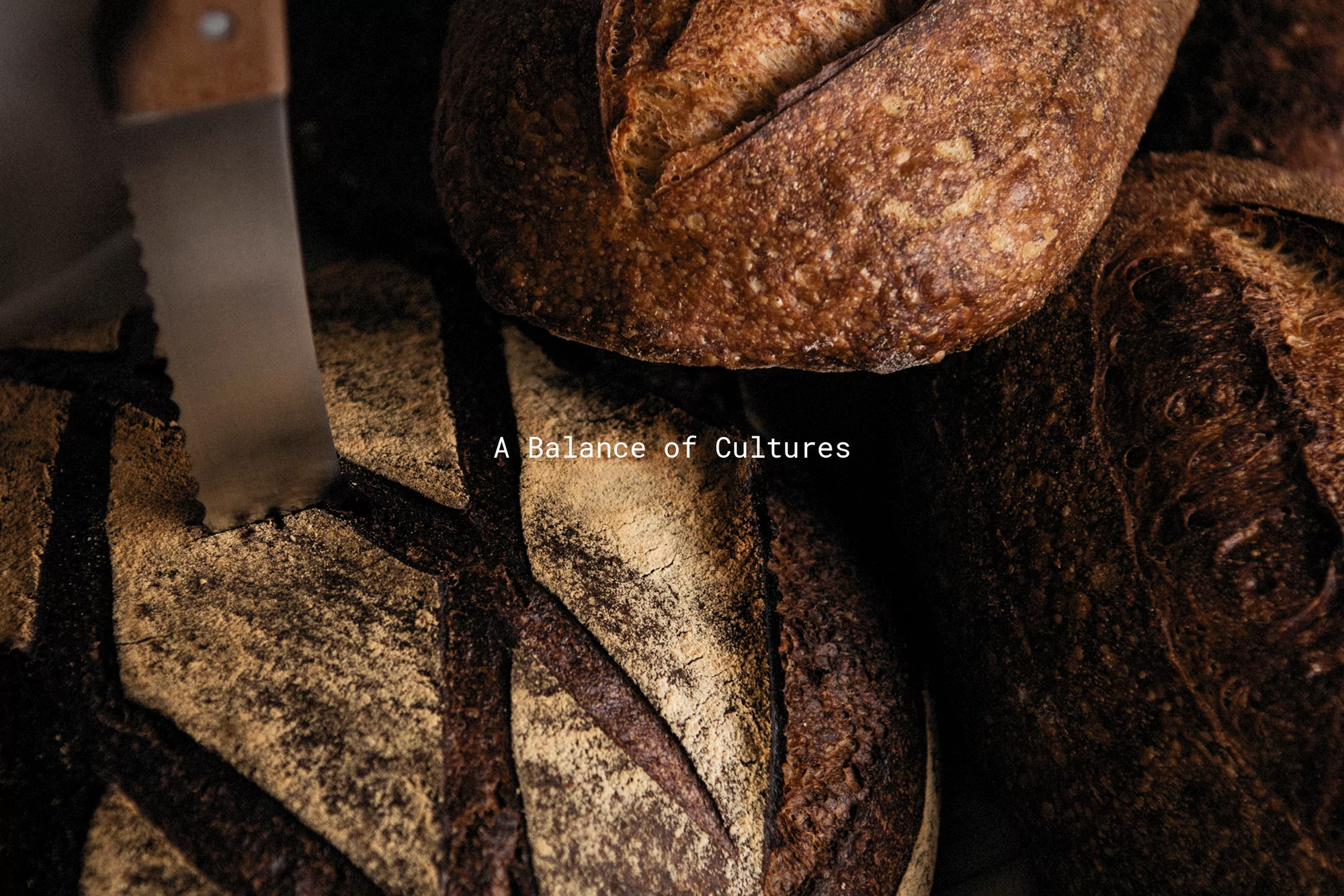 Close-up of artisanal sourdough bread loaves next to bread knife in dark food photography, emphasizing texture and crust detail.