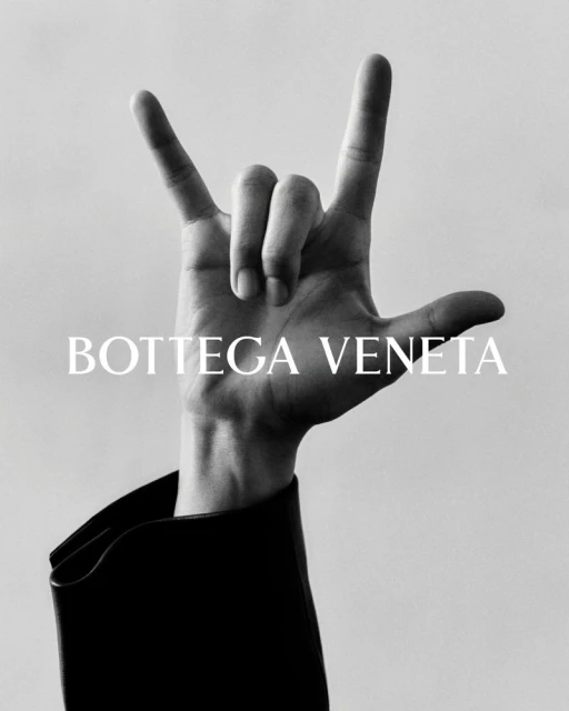 Hand makes rock and roll sign with fingers extended upwards. Designer black leather coat with Bottega Veneta text overlayed.