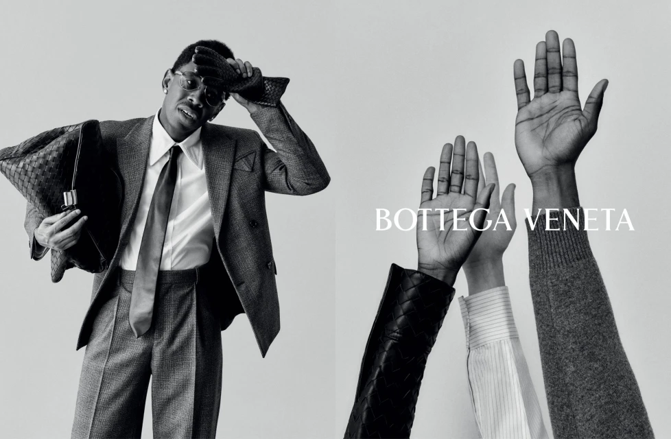 A man in a suit holding a woven leather bag is featured alongside a group of raised hands in a black and white fashion ad.