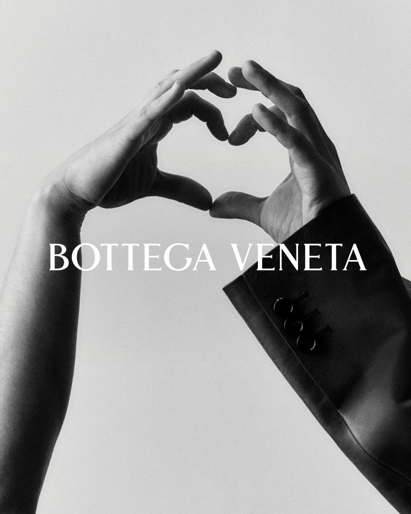 Black-and-white studio shot featuring two hands forming a heart shape near a Bottega Veneta blazer sleeve against a light backdrop.