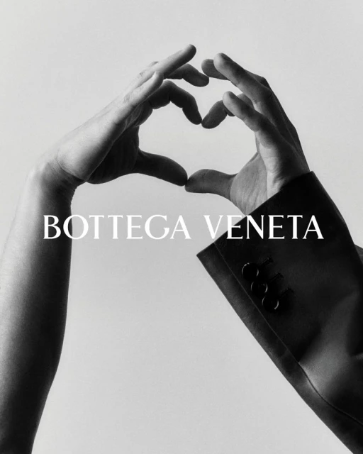 Black-and-white studio shot featuring two hands forming a heart shape near a Bottega Veneta blazer sleeve against a light backdrop.