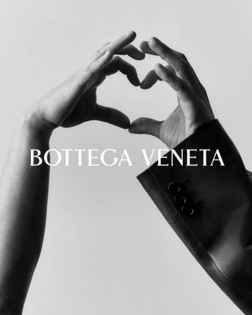 Black-and-white studio shot featuring two hands forming a heart shape near a Bottega Veneta blazer sleeve against a light backdrop.