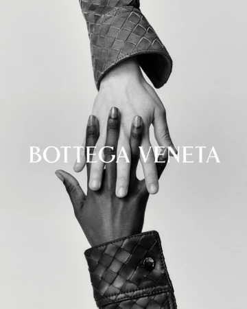 Interlocking hands in a black-and-white studio shot featuring Bottega Veneta woven leather cuffs, showcasing high-fashion textures.