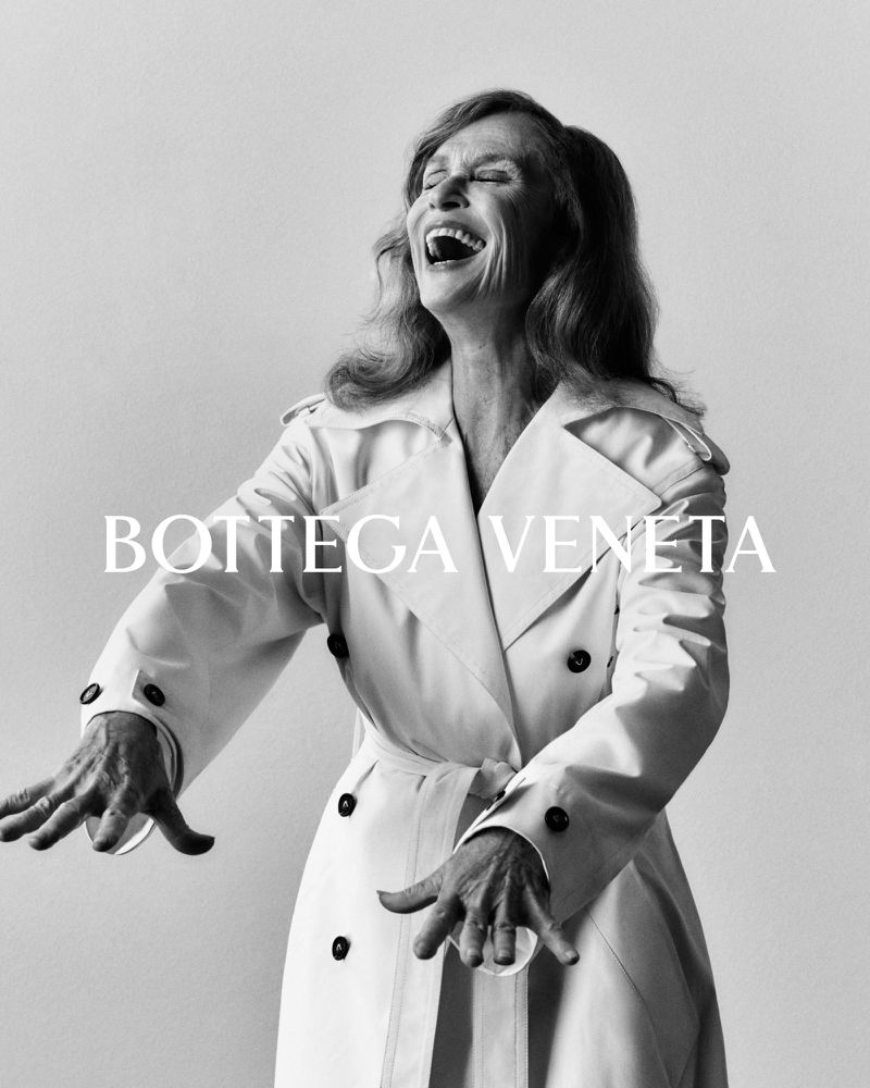 Black and white portrait of an adult woman laughing, wearing a white trench coat, set against a neutral background, featuring Bottega Veneta text.