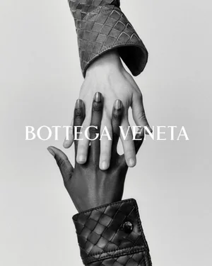 Monochrome close-up of two hands reaching and holding each other against a plain background wearing woven leather cuffs.