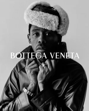 Portrait of Tyler, the Creator wearing a leather jacket and furry trapper hat against a plain background