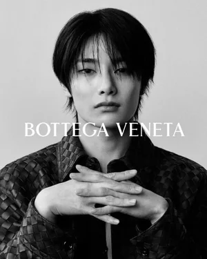 Black and white portrait of a person with dark hair wearing a woven leather jacket with overlaid brand text