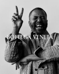 Black and white portrait of laughing man wearing woven leather jacket flashing peace sign for Bottega Veneta