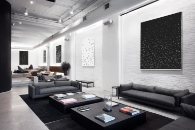 Spacious modern office lounge with white exposed brick walls, dark grey sofas, low black coffee tables, and contemporary art.