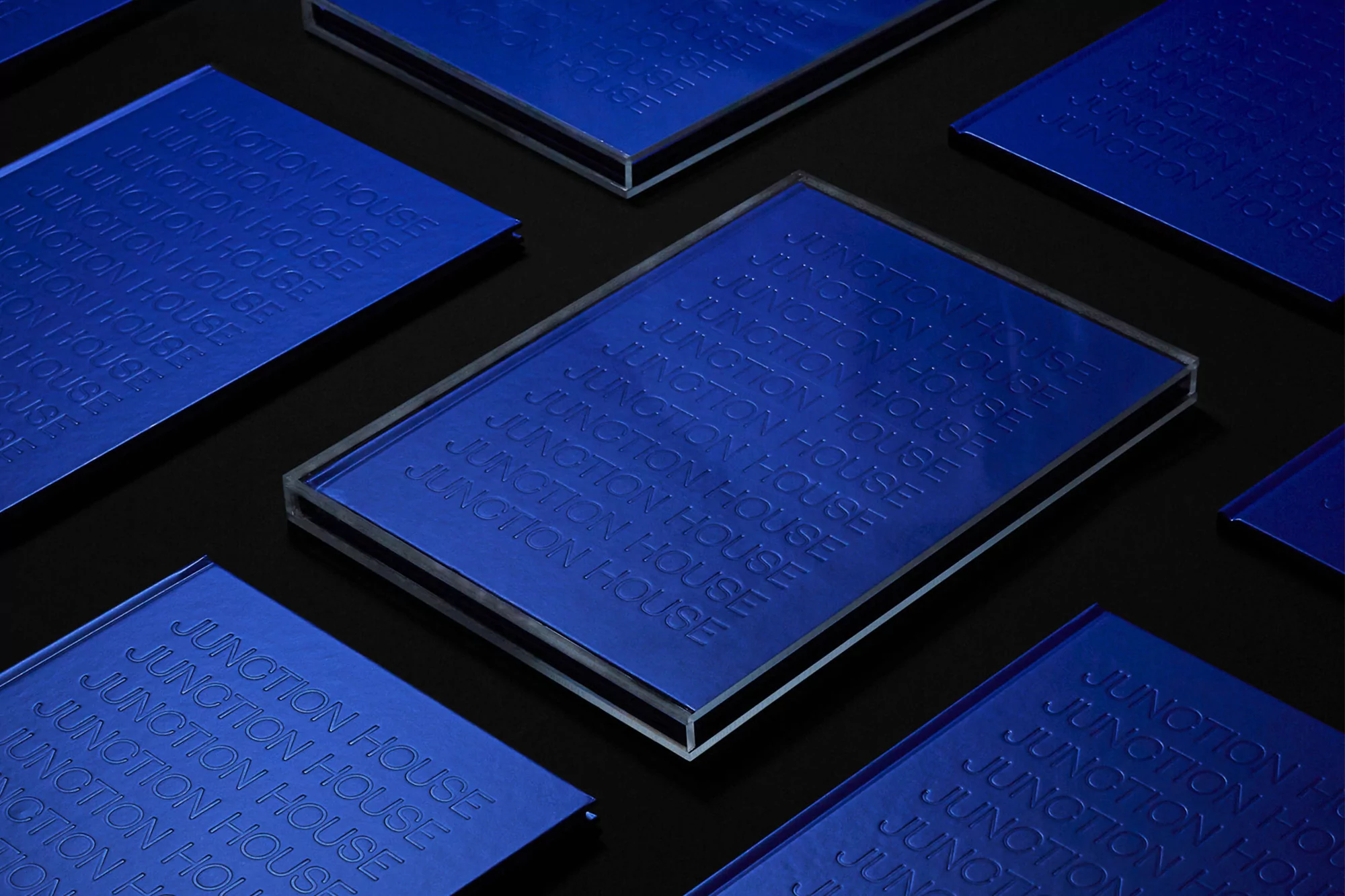 Close-up studio shot of multiple blue translucent plaques with 'Junction House' text, arranged diagonally on a black surface.