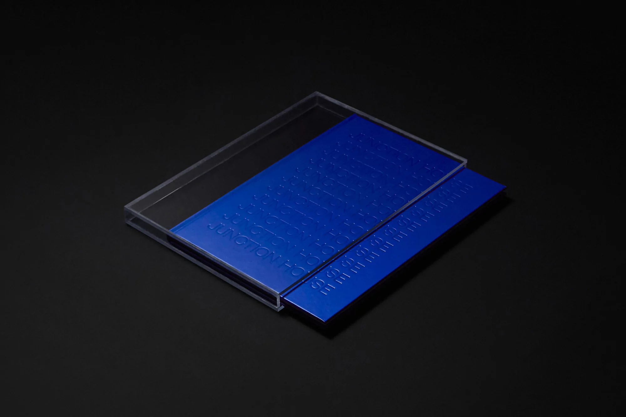 Elevated close-up of a cobalt blue embossed plastic case with sliding lid revealing text and patterns, set against a dark background.