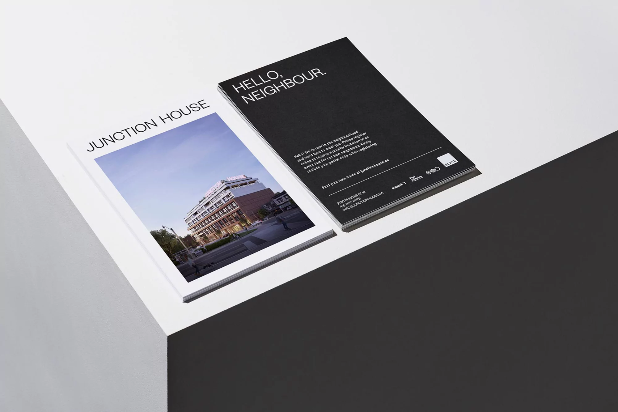Two booklets sit at an angle on a white and grey surface; one displays a building illustration, the other features text and a dark background.