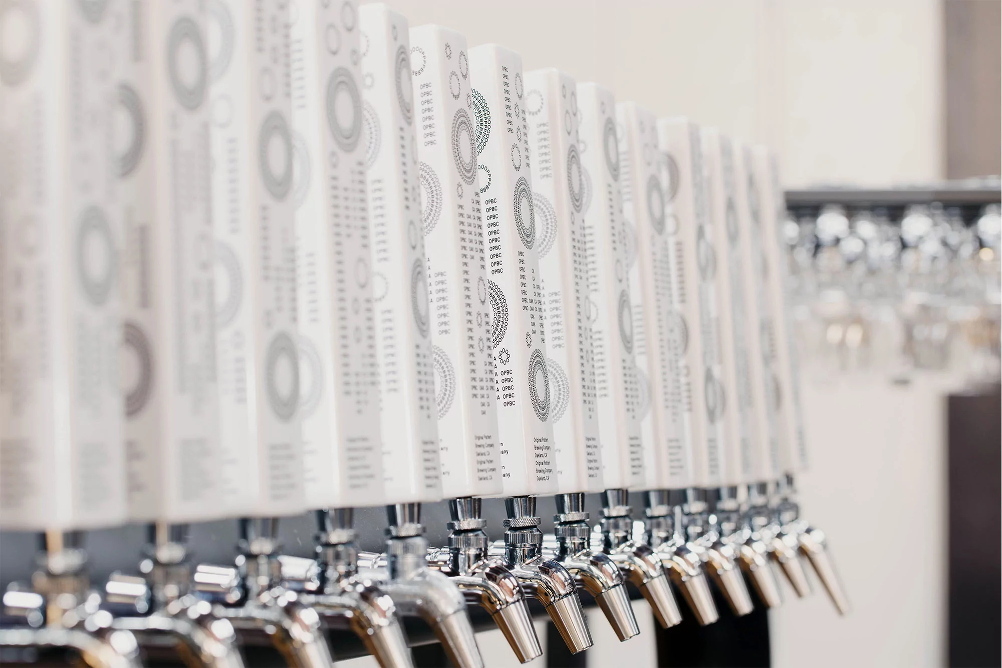 Row of chrome beer taps with white decorative handles in a bar setting, featuring a clean, modern aesthetic and blurred background.