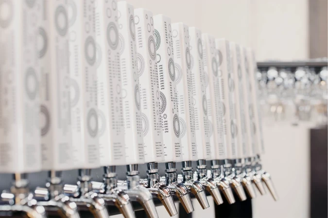 Row of chrome beer taps with white decorative handles in a bar setting, featuring a clean, modern aesthetic and blurred background.
