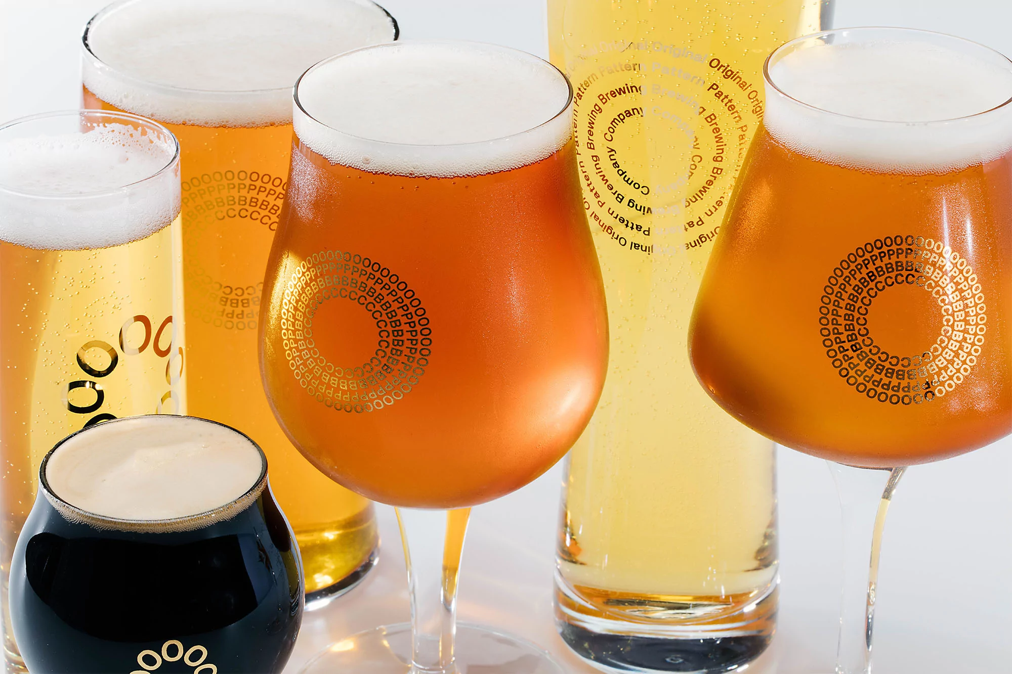 A collection of various beer glasses filled with different types and colors of beer, sitting against a white background.