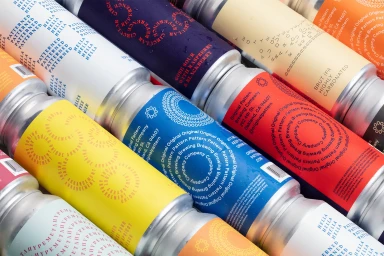 Close-up angled arrangement of colorful aluminum beverage cans featuring graphic typography labels and condensation droplets.