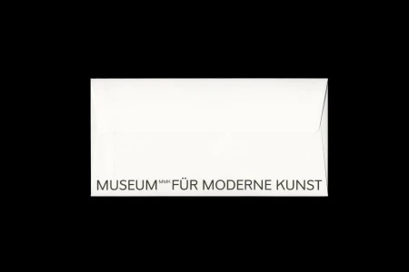 A white envelope centered on a solid black background, featuring the uppercase text MUSEUM FÜR MODERNE KUNST along the bottom edge.