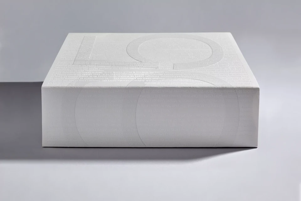 Minimalist product shot of a white, square box with subtle text and graphic design, set against a light gray background.
