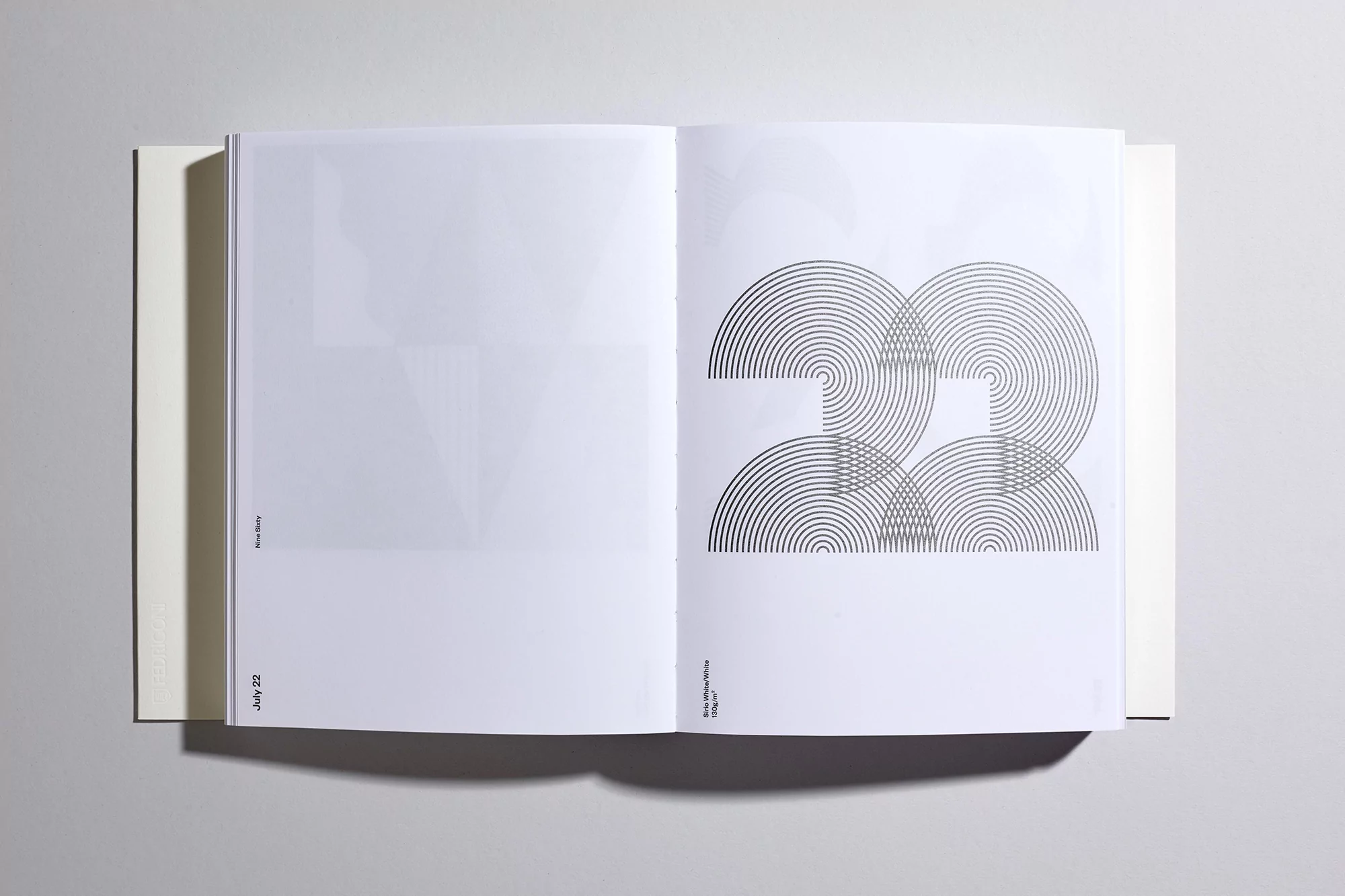 Open book displays graphic design with concentric circles creating an abstract image on a white page, presented in a minimalist style.
