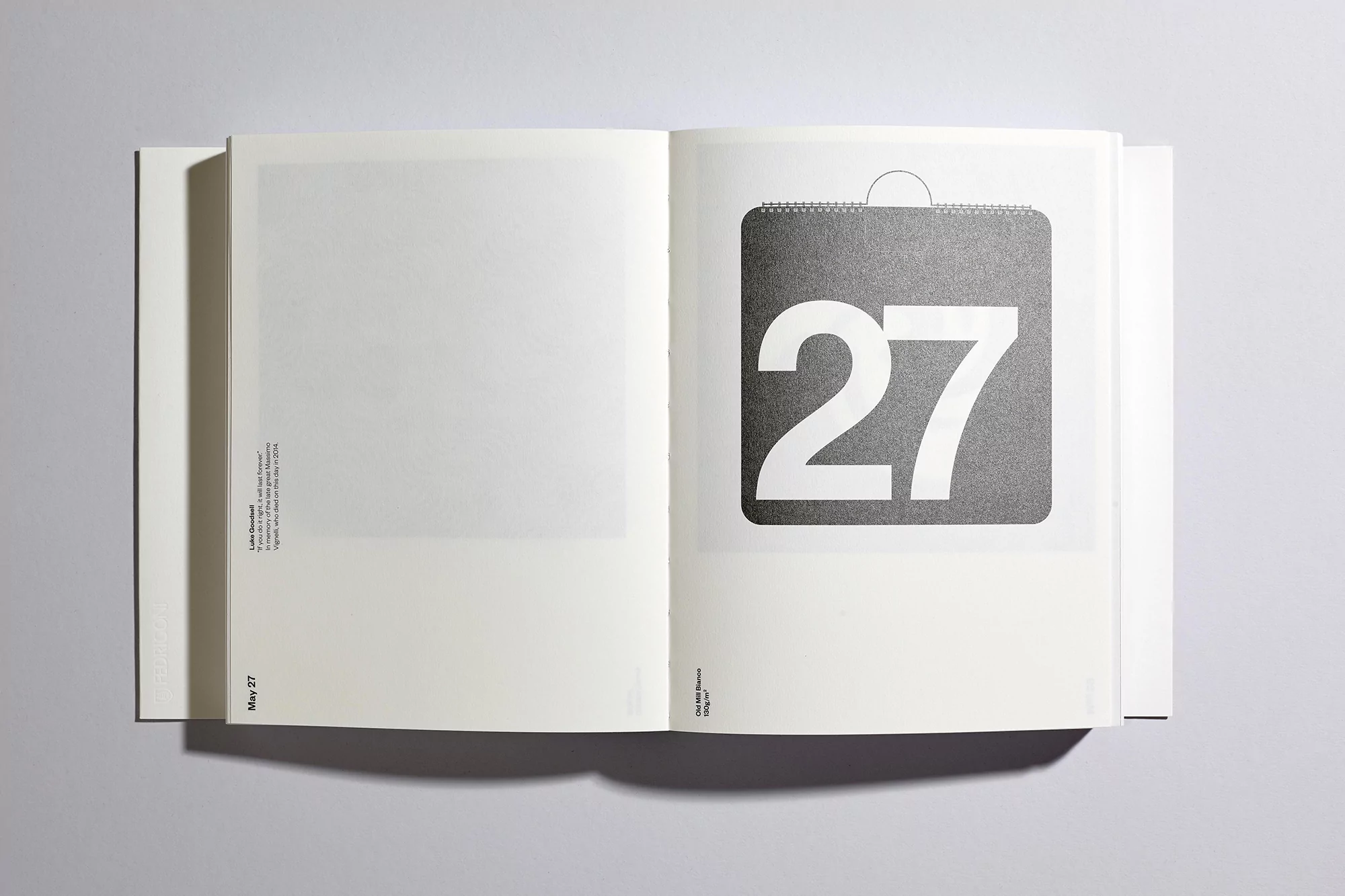 Open book on a white surface displays a calendar page with the number 27 in a bold, minimalist design, set against a gray square.